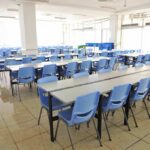 Empty cafeteria with rows of blue chairs and long tables