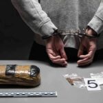‘Bible’ Bomb Manual Sparks Terror Case person in handcuffs behind back over table with seized packages
