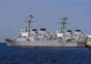 Three gray naval destroyers docked side by side at a pier
