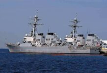 Three gray naval destroyers docked side by side at a pier