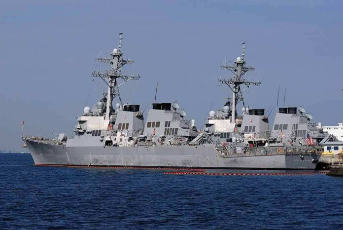 Three gray naval destroyers docked side by side at a pier