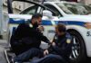 Two police officers by a patrol car, one injured and one calling for help