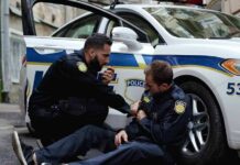 Two police officers by a patrol car, one injured and one calling for help