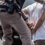 police officer handcuffing a person beside a vehicle