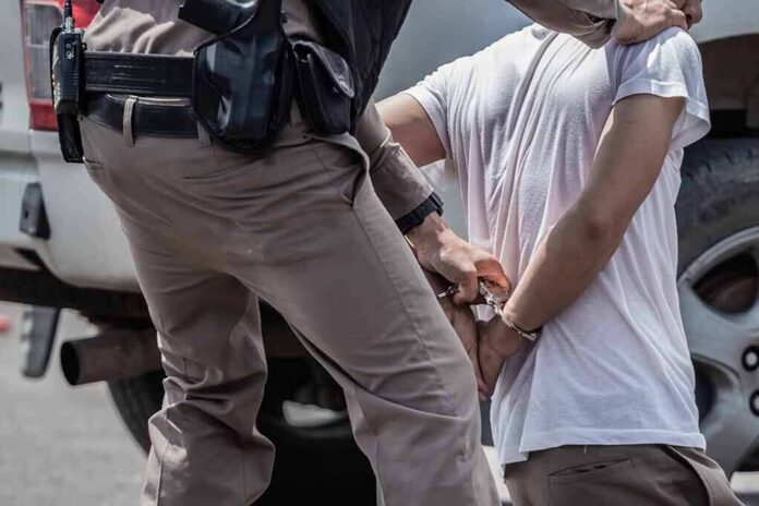 shutterstock_1705187374-1 police officer handcuffing a person beside a vehicle