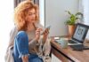 Woman using smartphone beside laptop on home desk