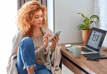 Woman using smartphone beside laptop on home desk