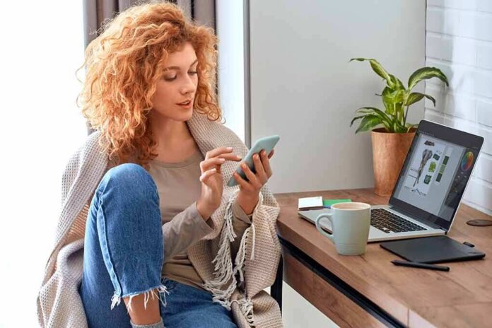 Woman using smartphone beside laptop on home desk