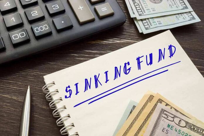 shutterstock_1981230602-1 Notebook labeled sinking fund beside cash, calculator, and pen