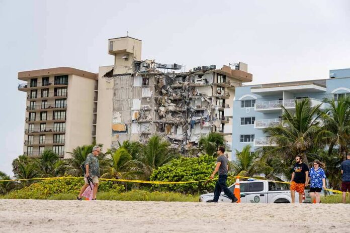 Partially collapsed beachfront apartment building behind people walking on sand