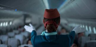 Flight attendant giving safety demonstration in airplane aisle