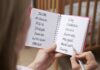 Hands holding a notebook with baby name lists near a crib