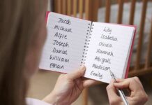 Hands holding a notebook with baby name lists near a crib