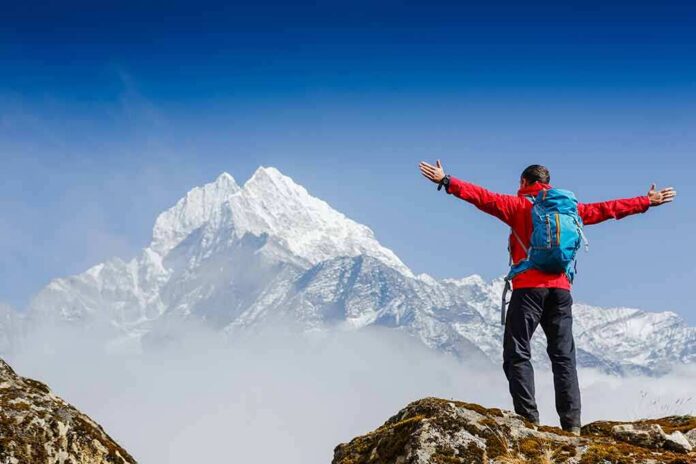 Hiker with arms raised facing snowy mountain peak