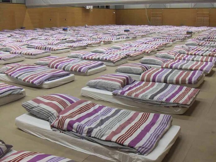 rows of mattresses with striped bedding in a large hall