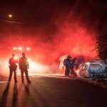 Firefighters and police at a nighttime car fire scene
