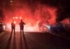 Bus Standoff Tied To Burning House Police officers watch firefighters extinguish a car fire at night