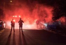 Police officers watch firefighters extinguish a car fire at night