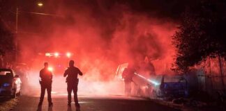Police officers watch firefighters extinguish a car fire at night