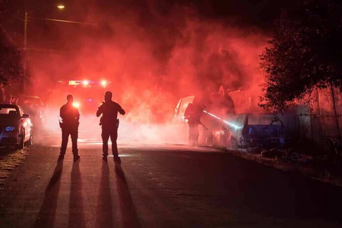 Police officers watch firefighters extinguish a car fire at night